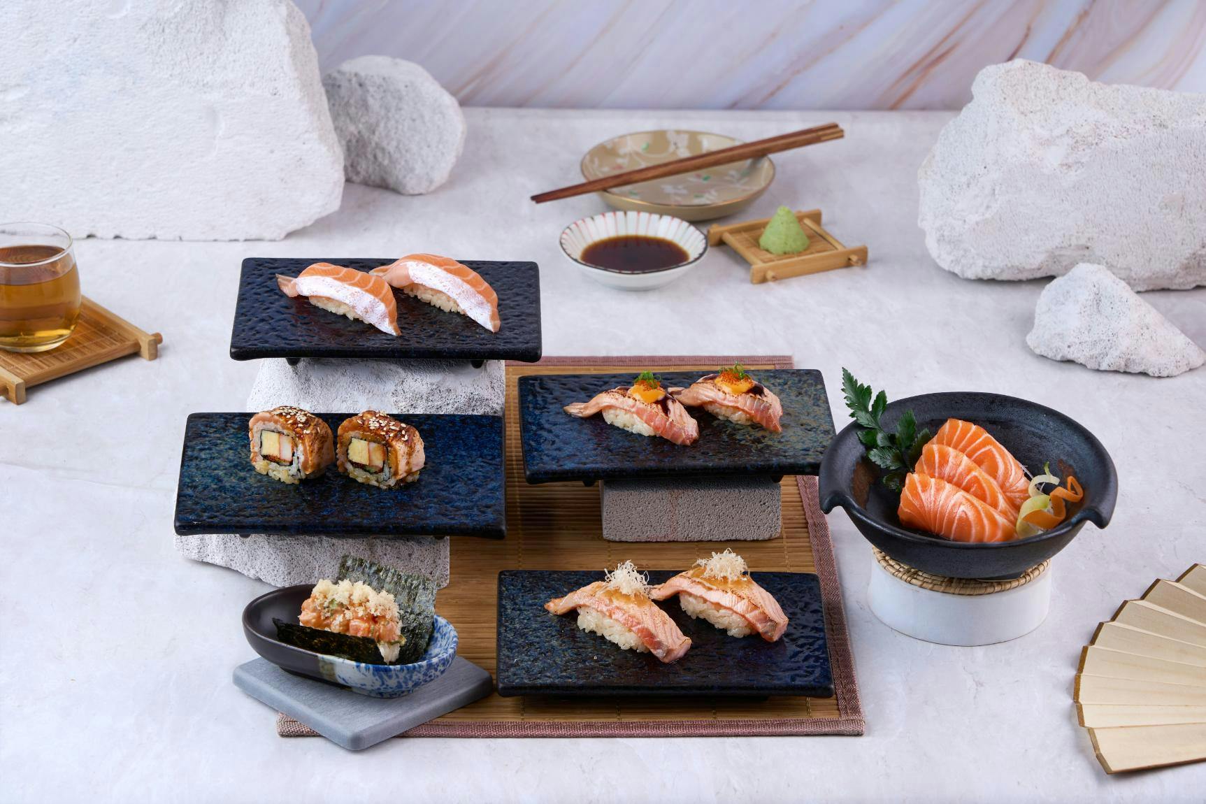 An assortment of sushi presented on black rectangular plates with chopsticks and condiments on a table.