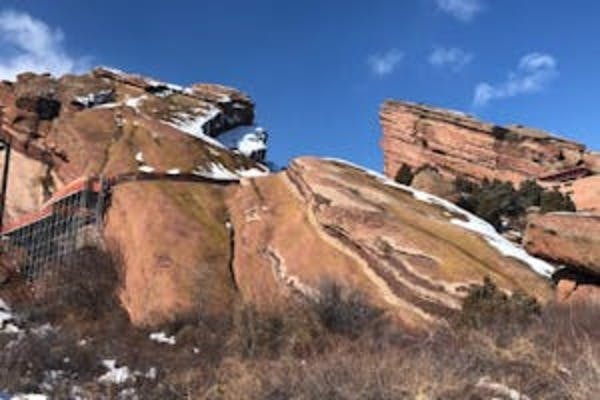 Formazioni rocciose rosse con chiazze di neve sotto un cielo azzurro e limpido. Vegetazione rada in primo piano.