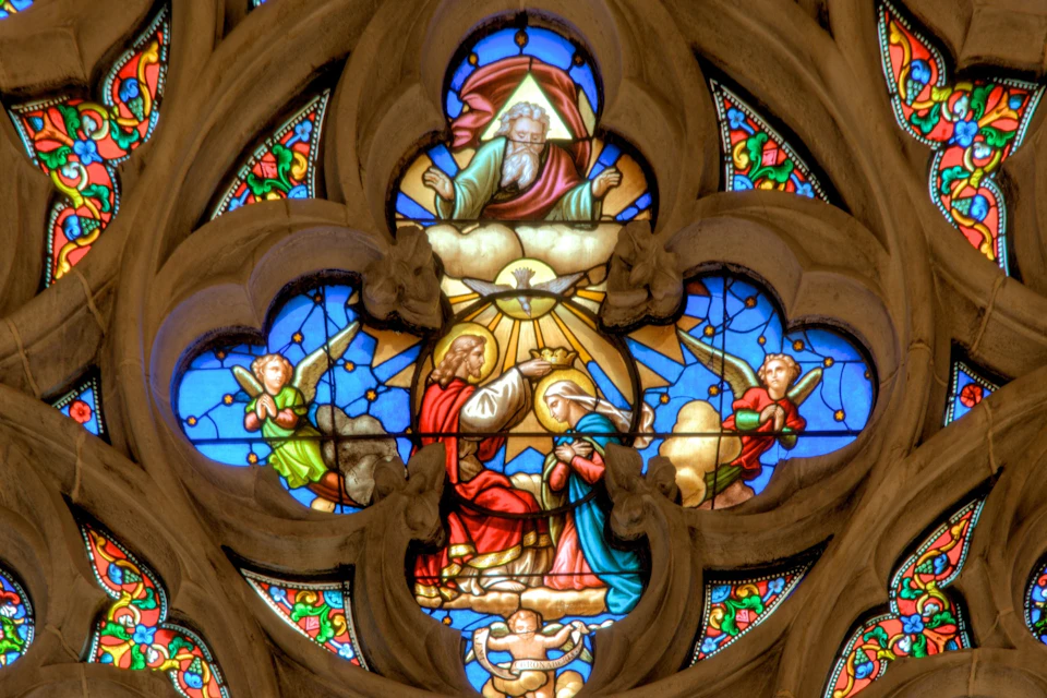 A stained glass window featuring a religious scene with figures, angels, and vibrant colors in an ornate design.