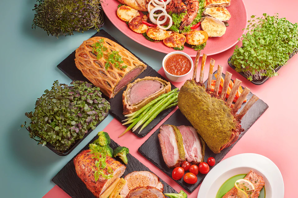 A selection of gourmet dishes including beef Wellington, rack of lamb, and roasted meats with vegetables and garnish.