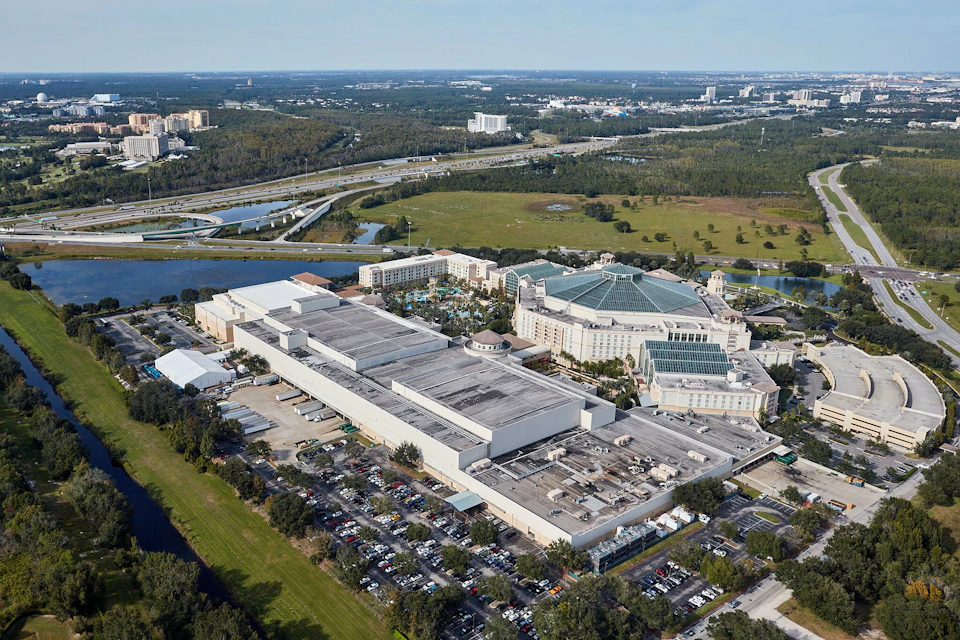 Aerial view of a large complex with rectangular buildings and a glass-domed structure, surrounded by parking lots and greenery.