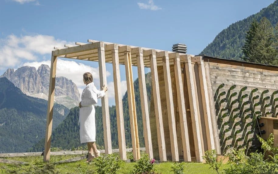 一个穿着白色长袍的人站在木制凉棚下，在晴朗的日子里俯瞰着山景。