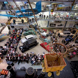 En flygbild av ett trångt museum med veteranbilar, flygplan och en varmluftsballongkorg upphängd från taket.