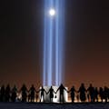 A group of people hold hands around the Imagine Peace Tower on Viðey Island.