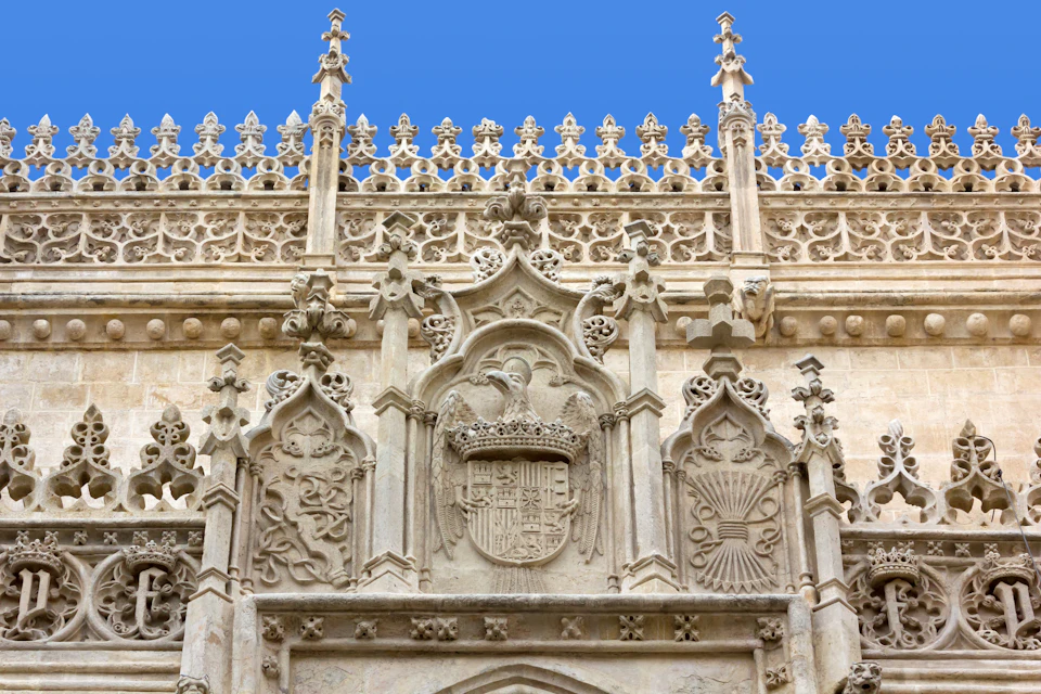 Elaborate stone facade of a Gothic-style building, featuring detailed carvings, a shield emblem, and ornamental spires.