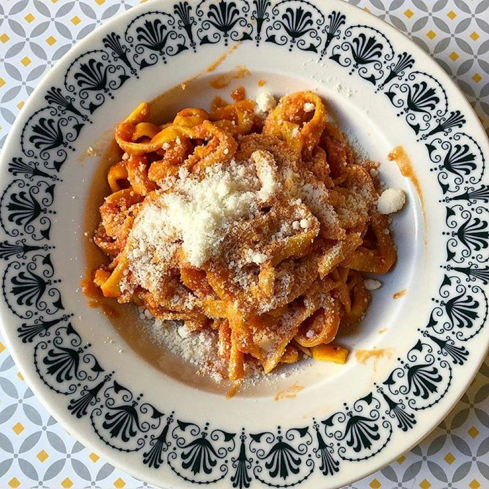 Πιάτο ζυμαρικών με σάλτσα ντομάτας, με τριμμένο τυρί, σερβιρισμένο σε περίτεχνο πιάτο με λευκά και μαύρα μοτίβα.