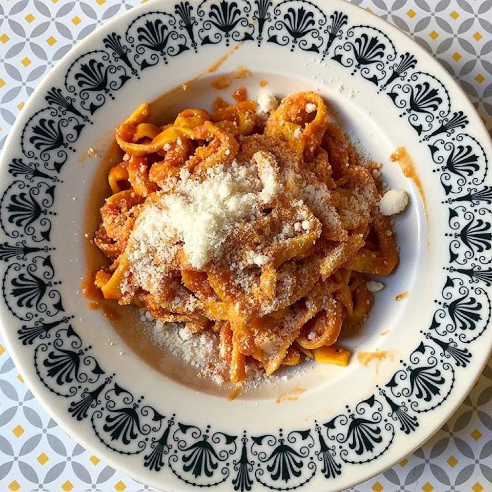 Plate of pasta with tomato sauce, topped with grated cheese, served on ornate white and black patterned dish.