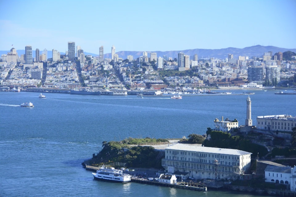 Skyline of a city with numerous buildings seen across a body of water, with a pier and boats in the foreground.