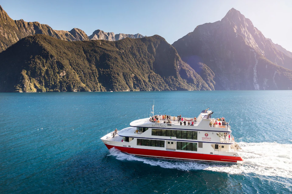 A red and white boat on a blue lake surrounded by mountainous terrain under a clear sky.