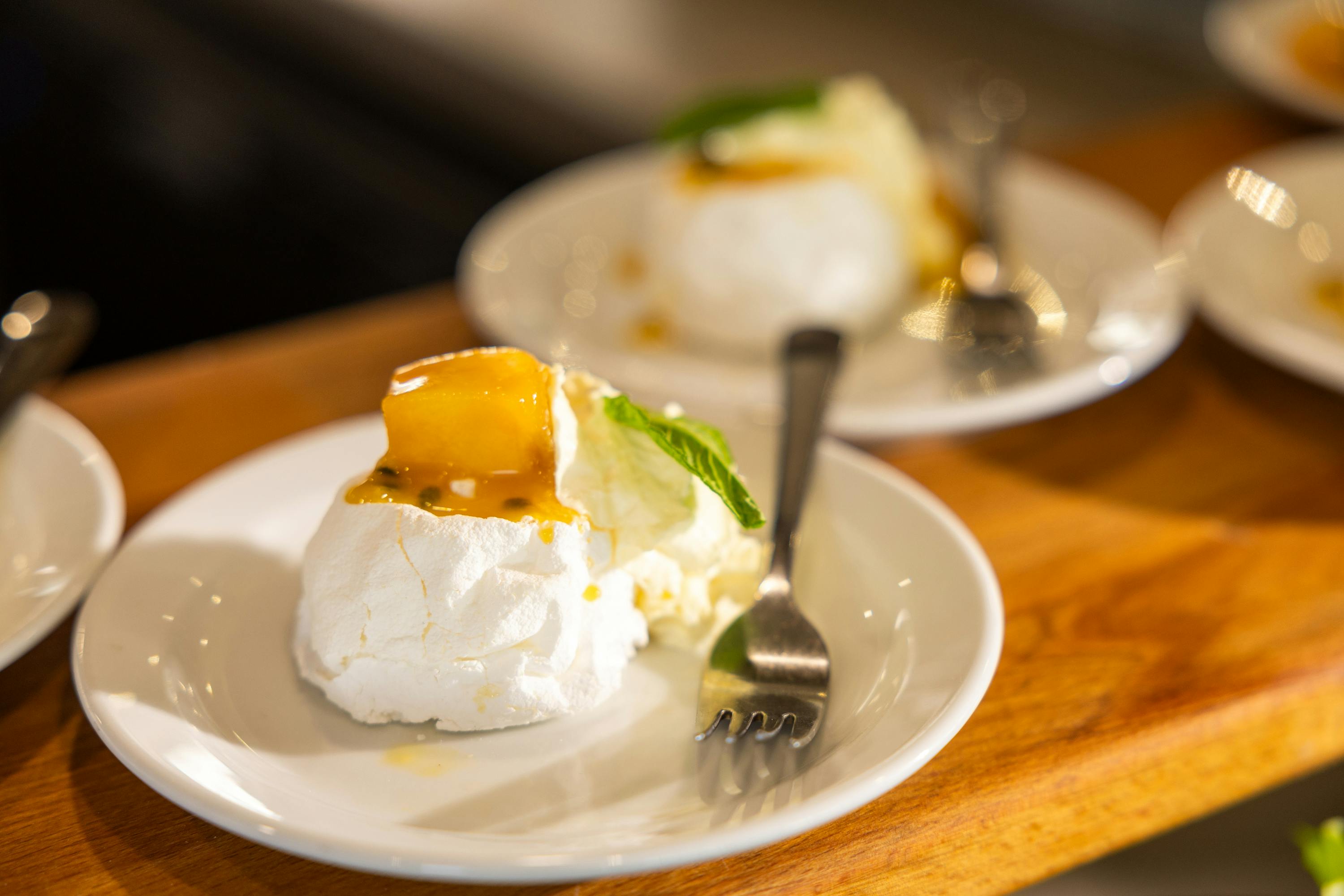 Δύο πιάτα πάβλοβα με σαντιγί, σάλτσα φρούτων του πάθους και ένα φύλλο μέντας, το καθένα με ένα πιρούνι ακουμπισμένο στο πιάτο.