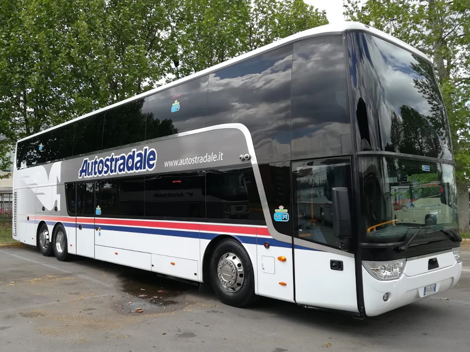 Double-decker bus with "Autostradale" branding, parked on a street with trees in the background.