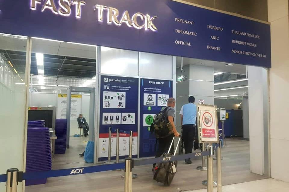 Two travelers pulling luggage enter a fast-track airport security lane marked for priority passengers.