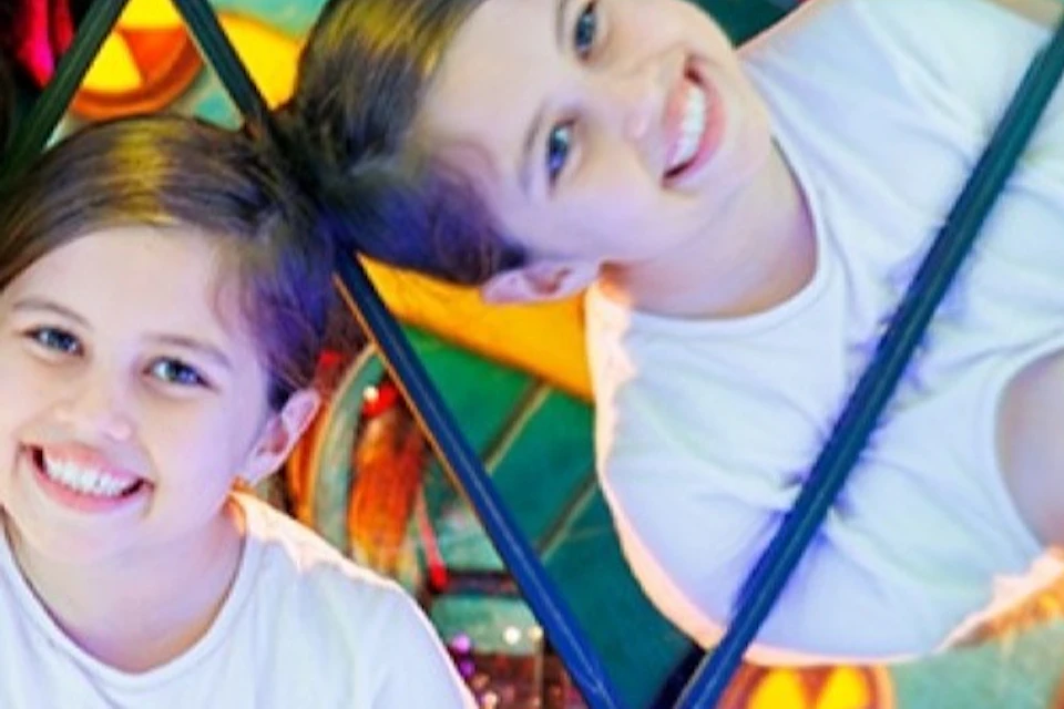 A smiling child reflected multiple times in a colorful mirrored environment with bright lights.