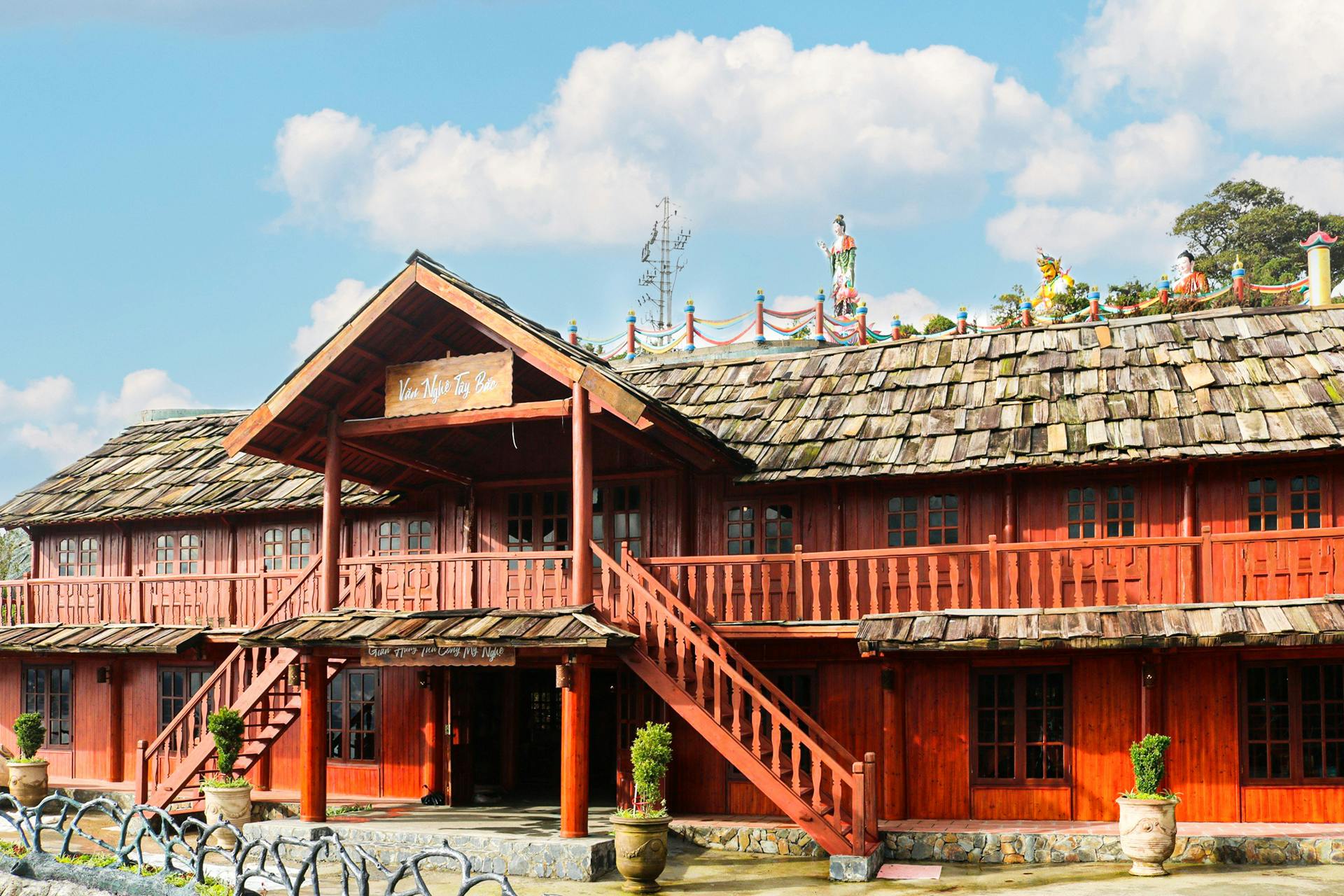 A two-story wooden building with a tiled roof, external staircase, and decorative elements under a bright sky.