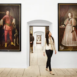 Två personer i en museigång beundrar stora porträtt av historiska figurer; en tredje person är i bakgrunden.