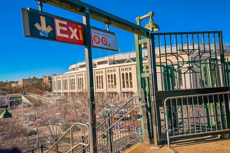 Exit sign and stairs leading down from a platform with Yankee Stadium in the background under a clear blue sky.