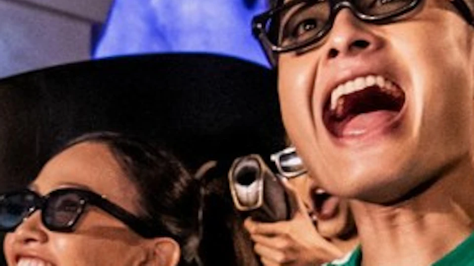 Group of people wearing 3D glasses, smiling and holding laser guns in an indoor amusement ride setting.