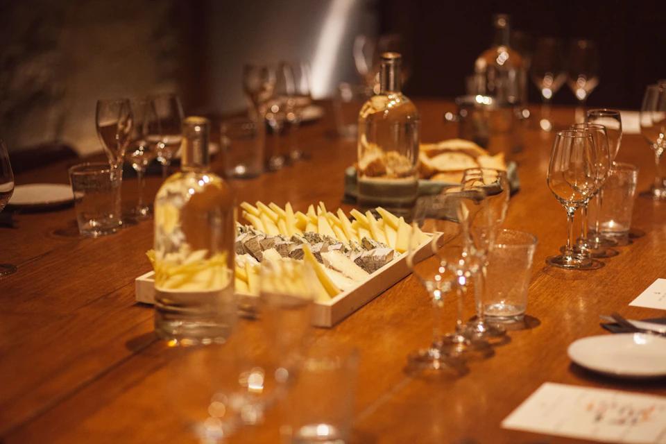 A table set with wine glasses, bottles, a cheese platter, and bread, creating a cozy dining ambiance.