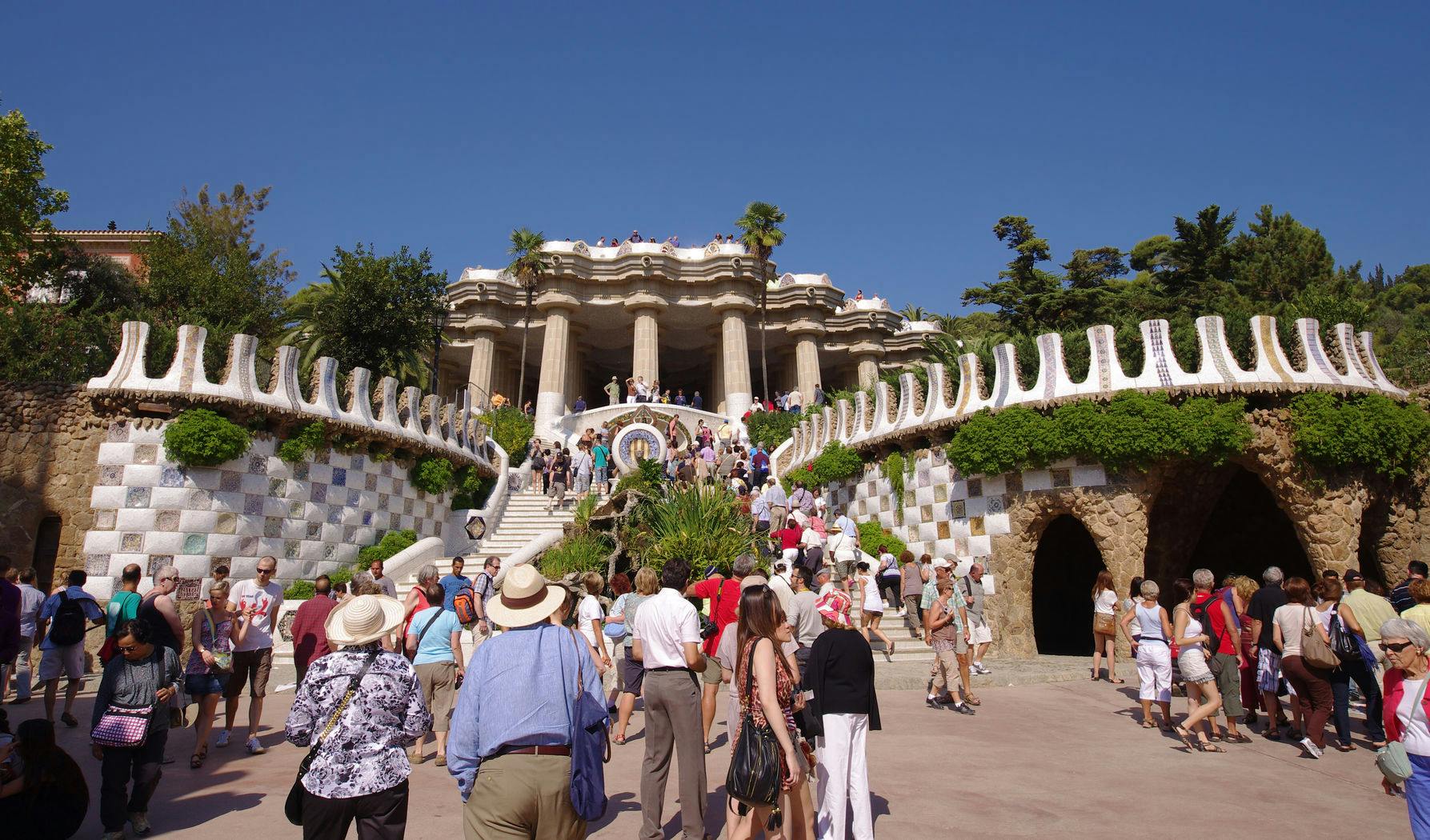 Un grand groupe de personnes monte de larges escaliers flanqués de murs décorés et de verdure, menant à une structure ornée de colonnes.