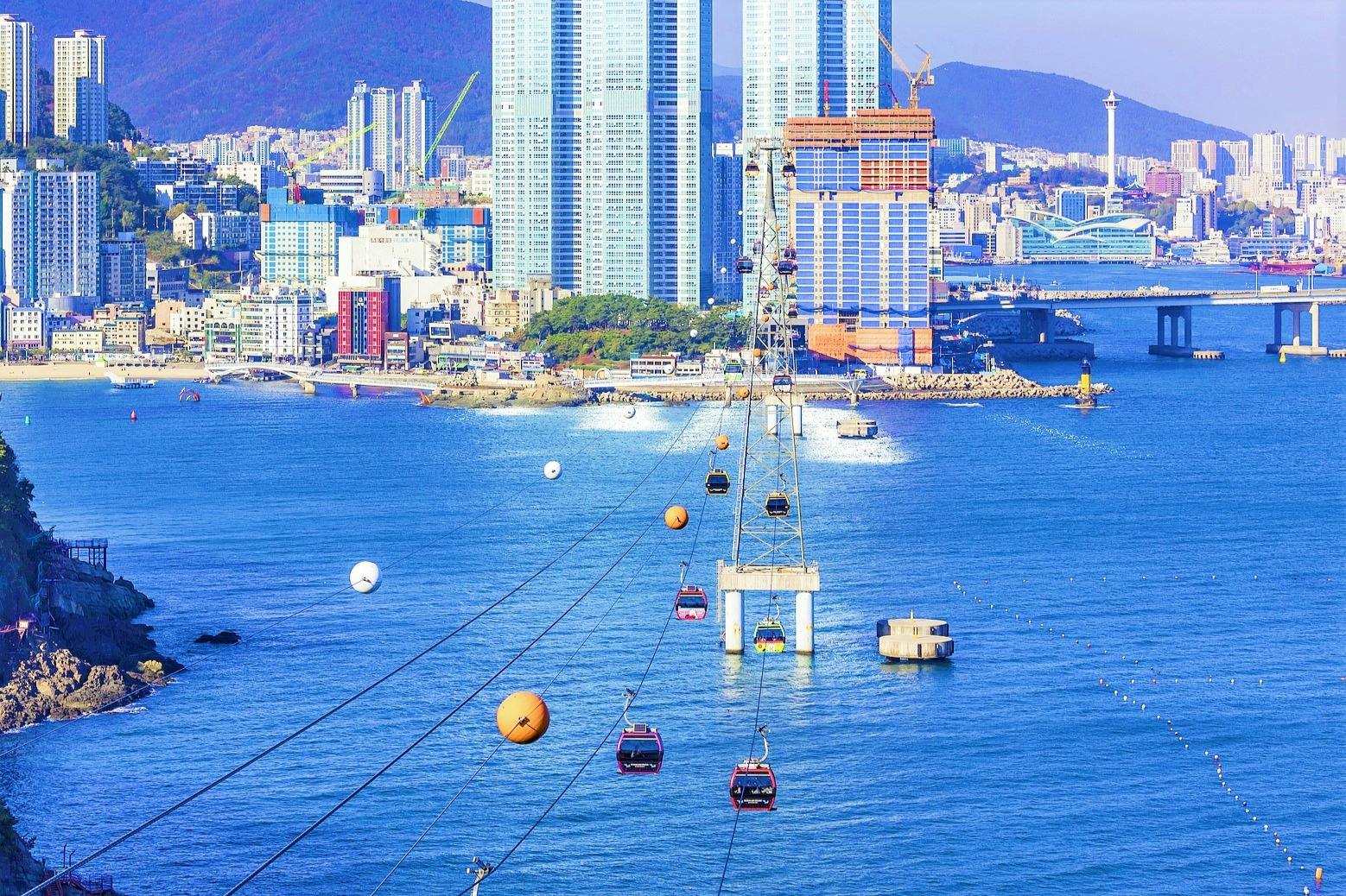 Cable cars cross over a body of water with a city skyline and tall buildings in the background.