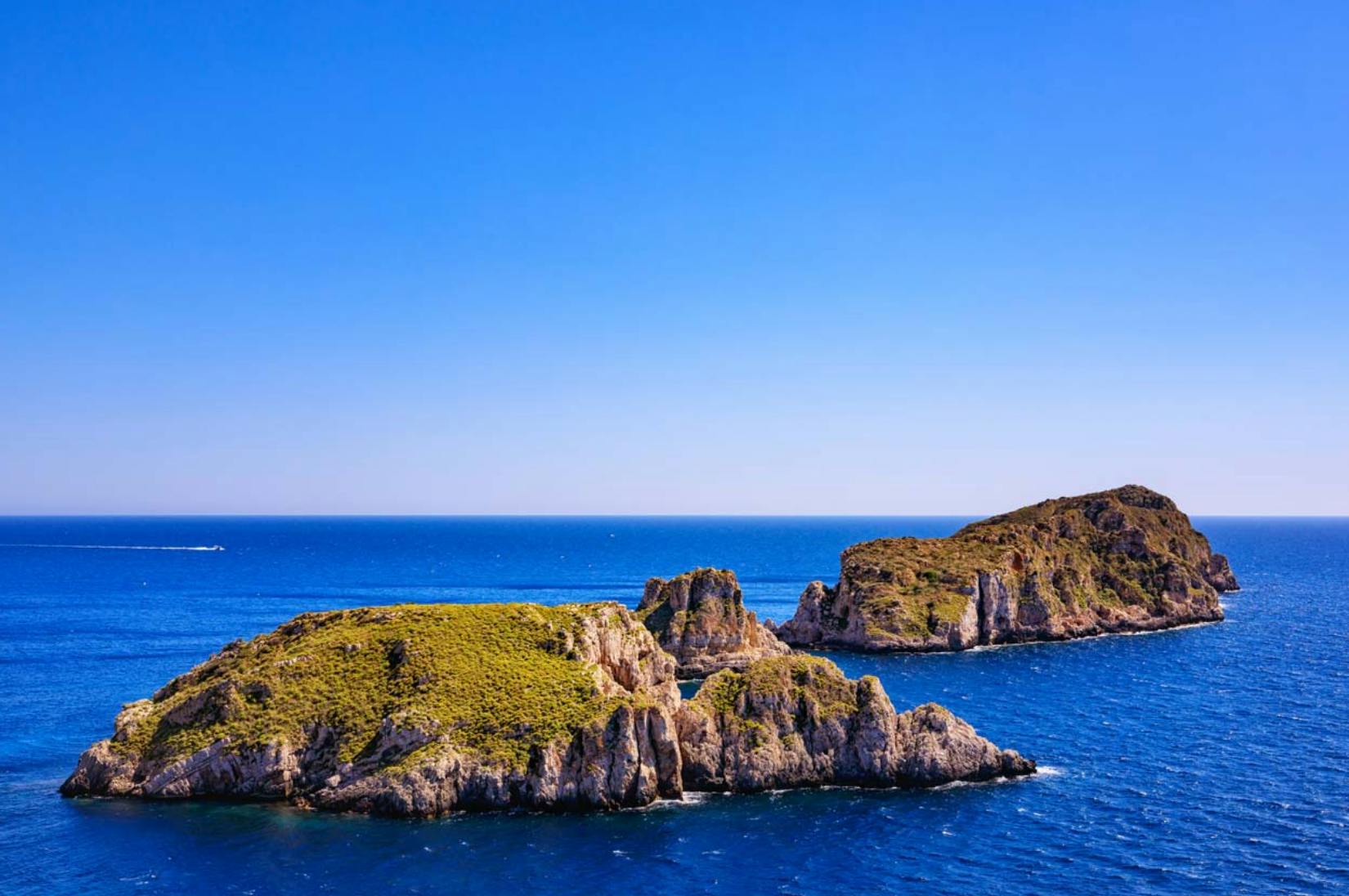 Eine malerische Aussicht auf felsige Inseln mit grüner Vegetation, umgeben von blauem Meer unter einem klaren, sonnigen Himmel.