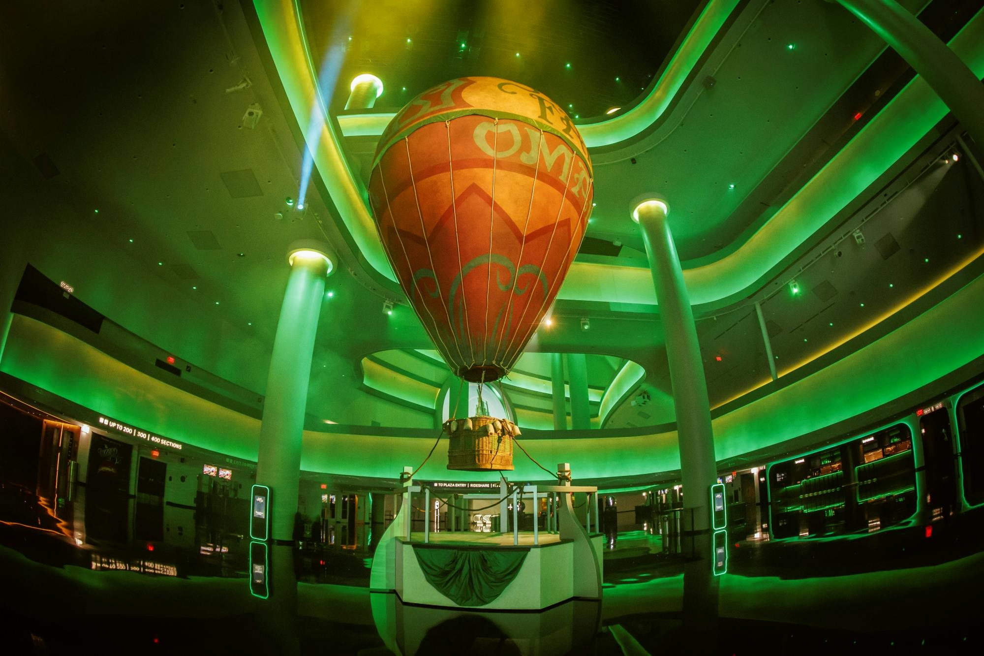 A colorful hot air balloon suspended indoors amidst green lighting with a modern architectural background.