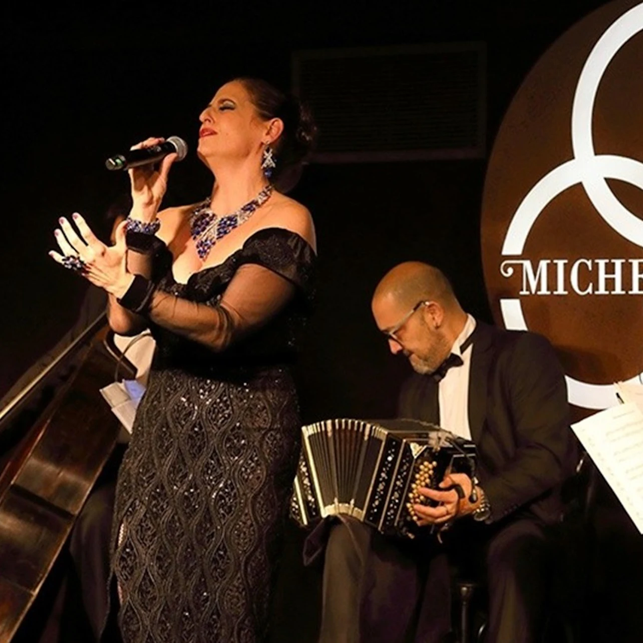 A captivating woman tango singer graces the stage, her voice weaving through the vibrant melodies of skilled musicians.