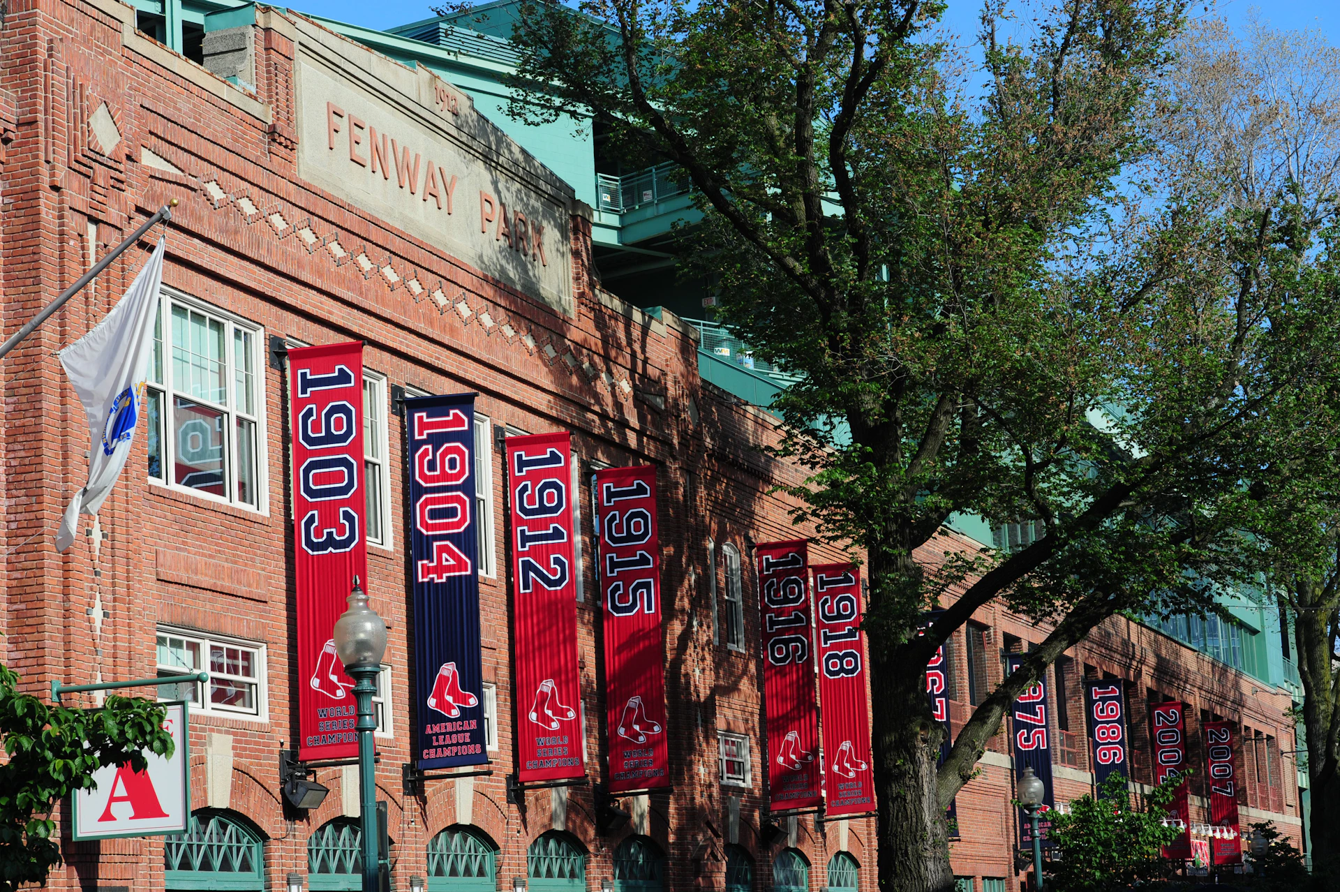 Exterior of Fenway Park with championship banners for the Boston Red Sox ranging from 1903 to 2018, and trees in the foreground.