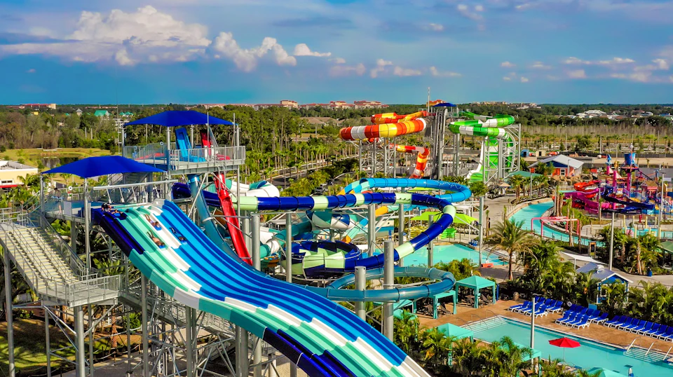 Colorful water park with multiple twisting slides and pools, set against a backdrop of trees and a partly cloudy sky.