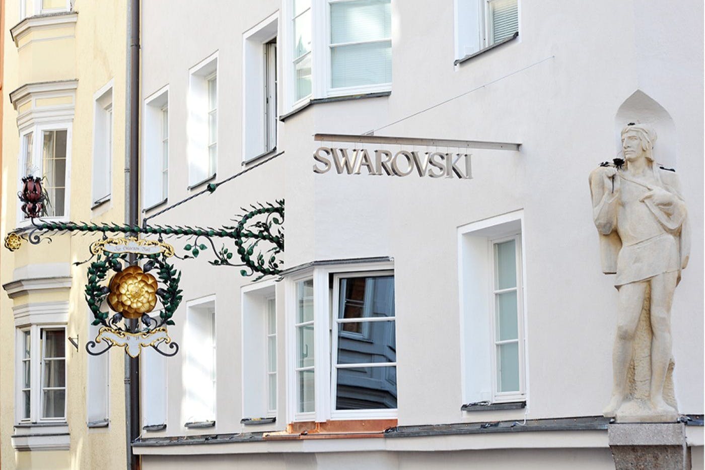 一座石头雕像矗立在建筑物的角落，设有几扇窗户和"施华洛世奇"标志。