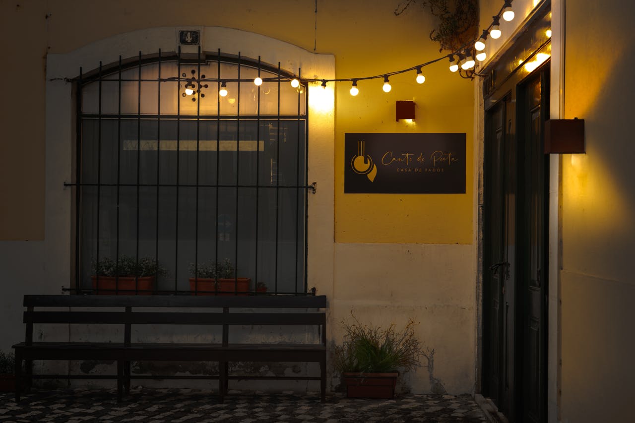 ストリングライト付きの屋外カフェ、「Canto da Peia」と書かれた看板、バー、フラワーポット、ベンチ付きの窓。