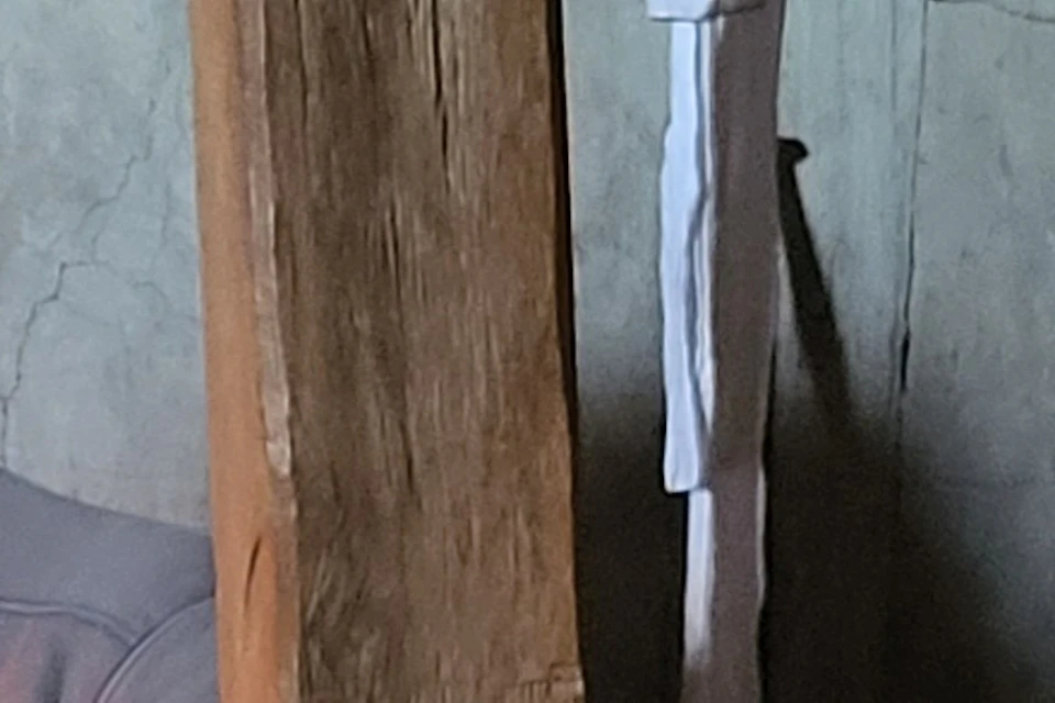 Two women in historical clothing in a rustic interior. One plays a wooden flute while the other tends to a fireplace.