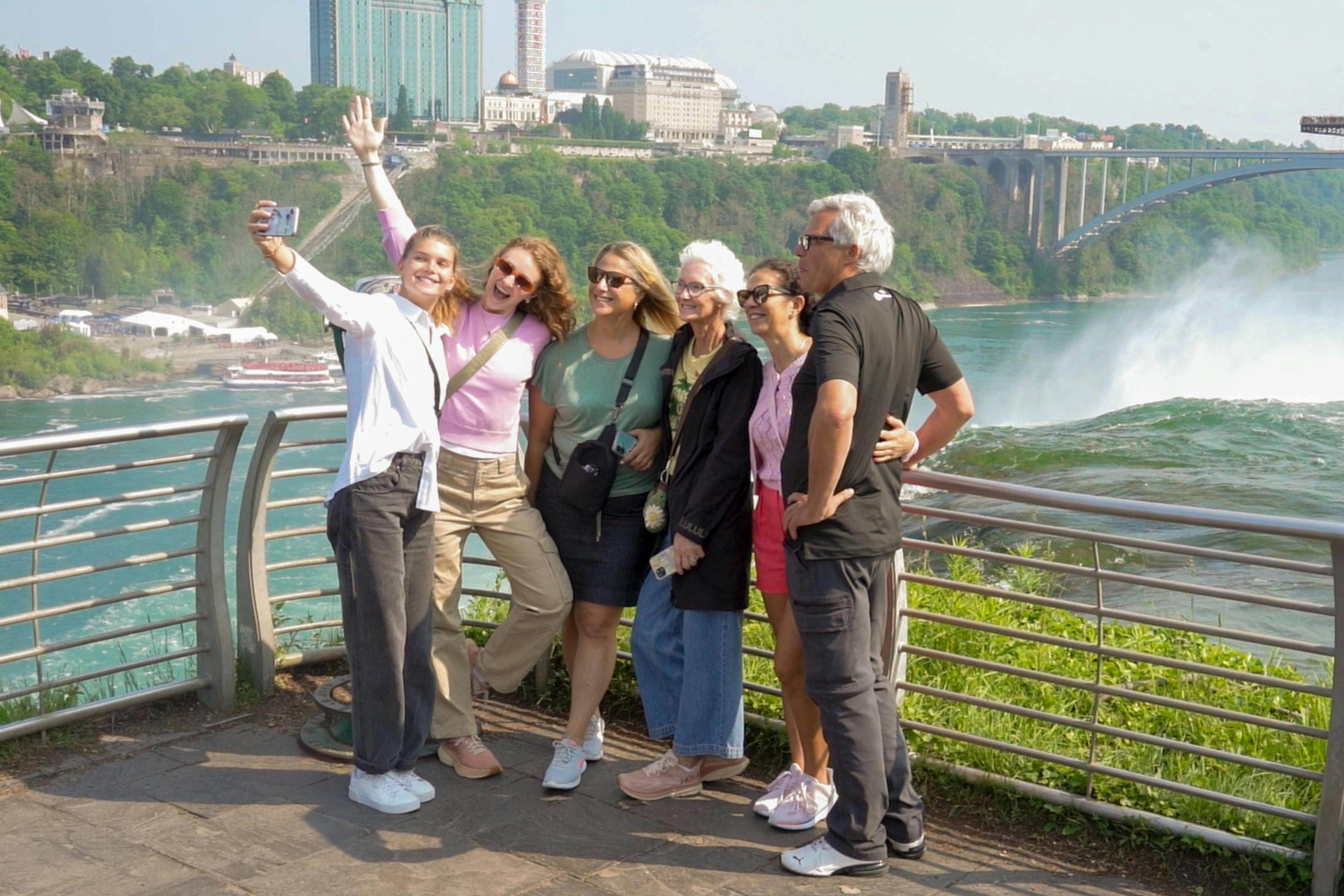 여섯 명이 도시, 나무, 물을 배경으로 아름다운 전망을 배경으로 미소를 짓고 셀카를 찍고 있습니다.