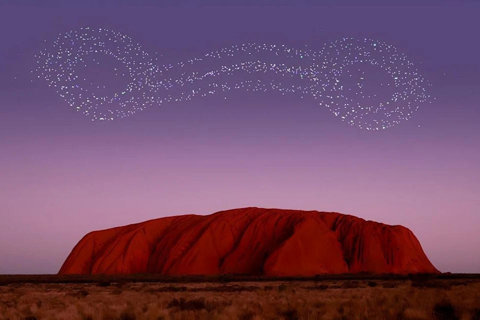 A large red rock formation under a purple sky with bright stars forming swirling patterns above it.