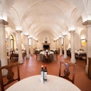 An elegant restaurant with vaulted ceilings, stone columns, and neatly arranged tables set with white tablecloths and bottles of olive oil.