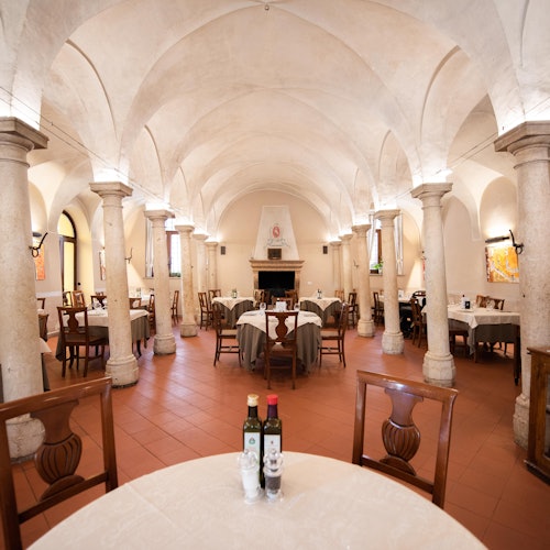 An elegant restaurant with vaulted ceilings, stone columns, and neatly arranged tables set with white tablecloths and bottles of olive oil.