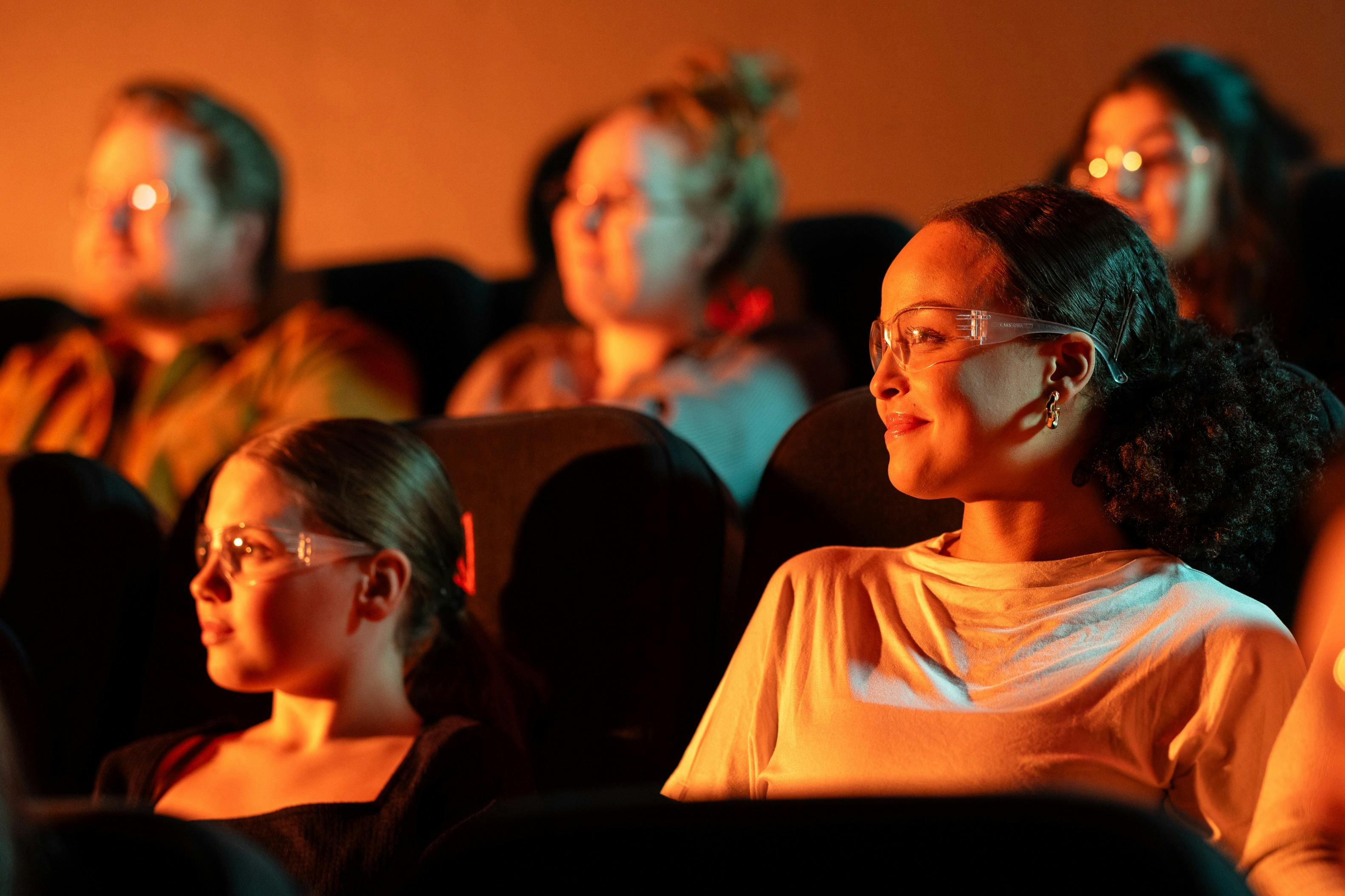 A girl and her mother watch the Lava Show. They are wearing safety goggle. Other people are in the background.