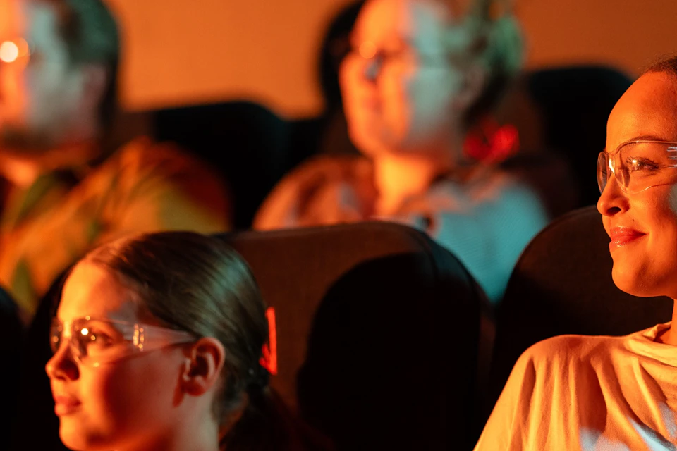 A girl and her mother watch the Lava Show. They are wearing safety goggle. Other people are in the background.