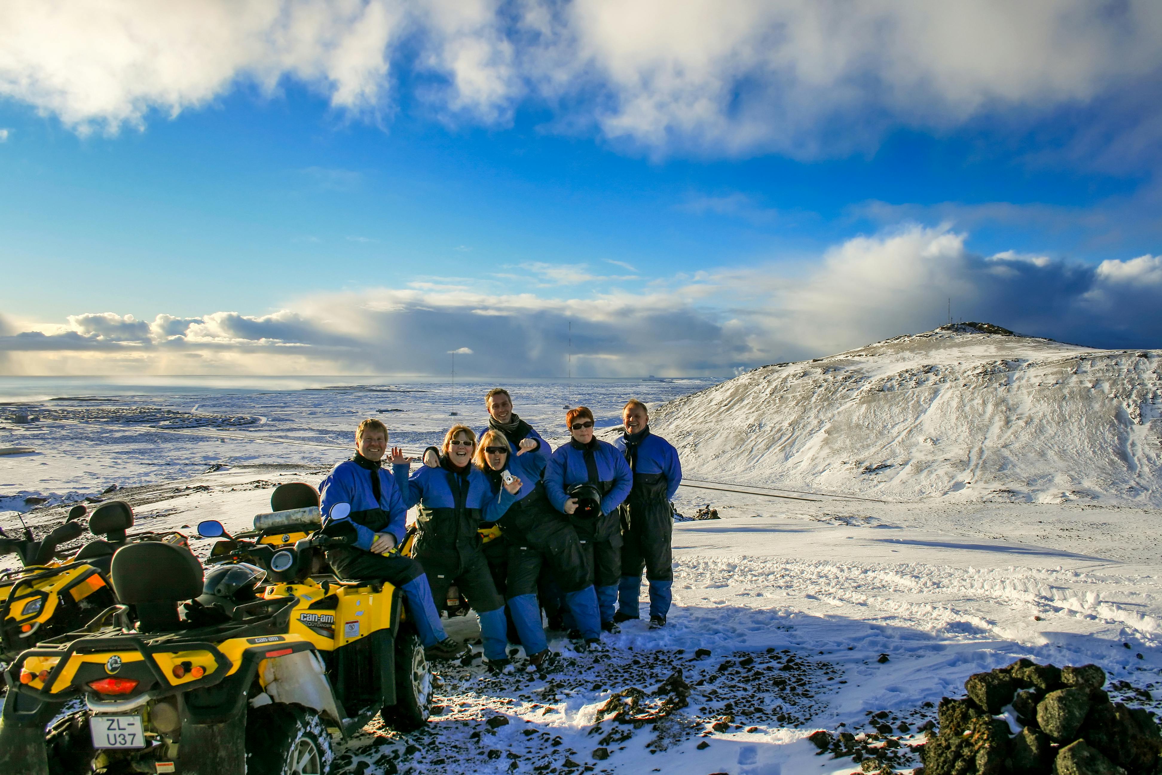 Groupe de six personnes en combinaison bleue à côté d'un VTT jaune dans un paysage de collines enneigées sous un ciel bleu.