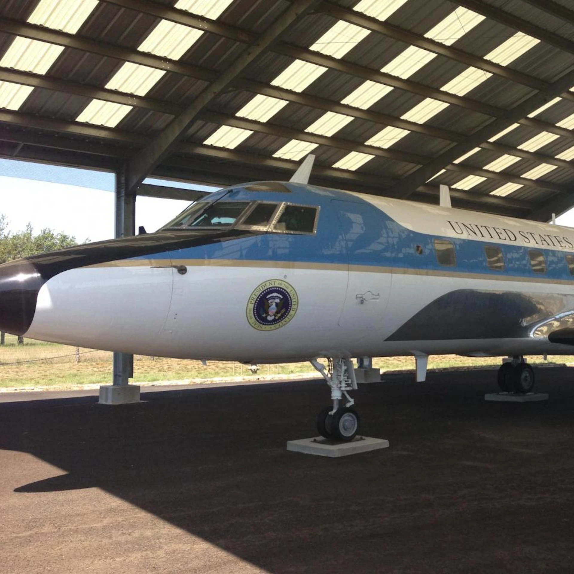 A blue and white airplane with "United States" and a presidential seal, parked under a roofed structure.