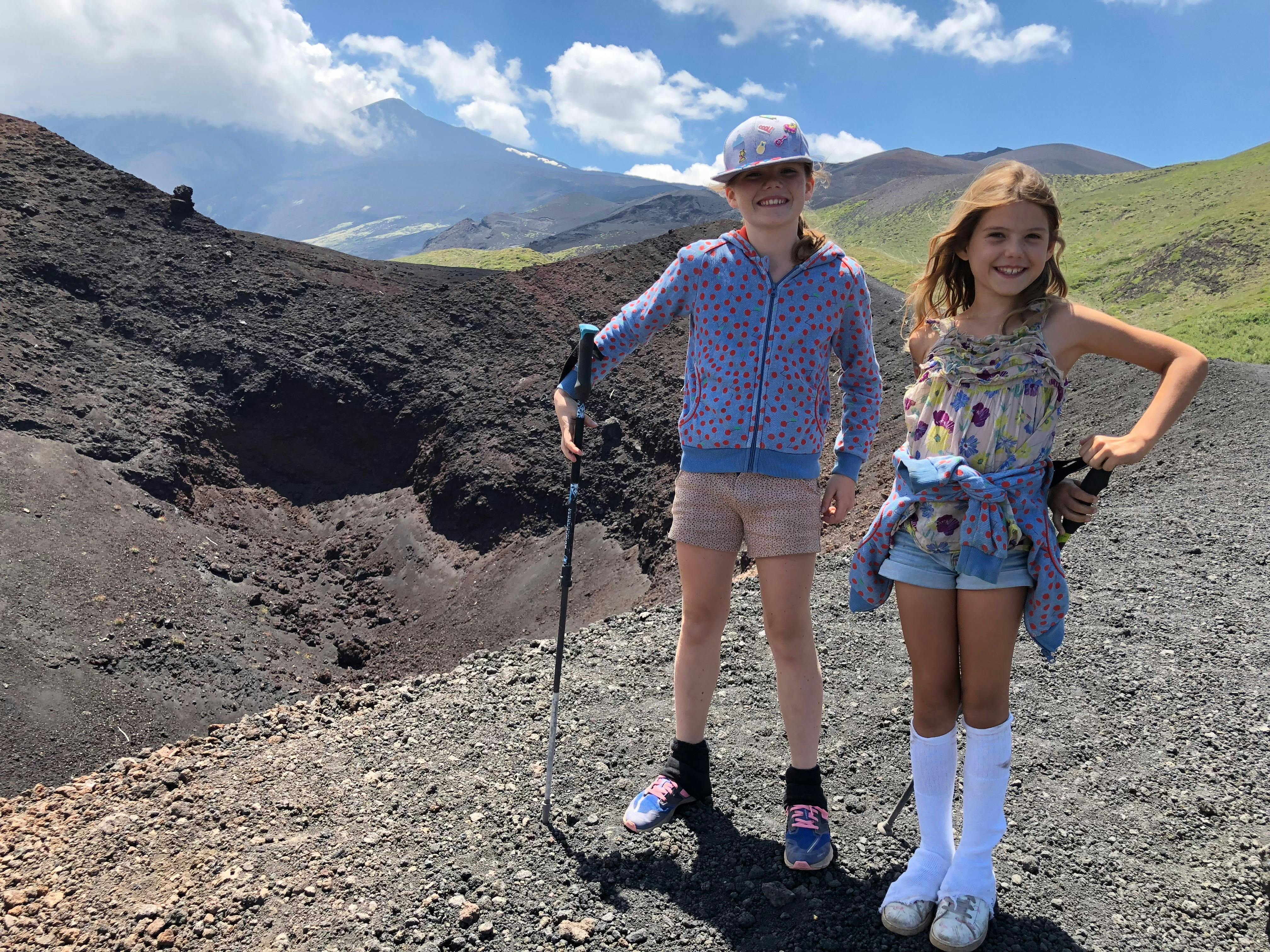 밝은 푸른 하늘 아래 산을 배경으로 바위 지형에 서 있는 캐주얼한 옷을 입은 미소 짓는 두 소녀.