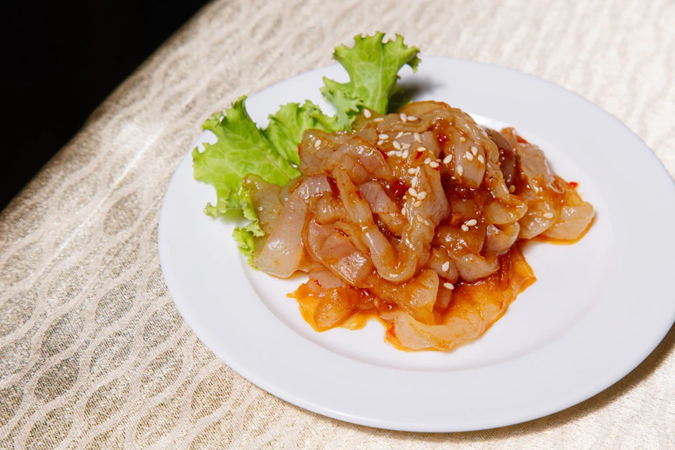 A dish of marinated sliced meat with sesame seeds, served on a lettuce leaf, presented on a white plate.