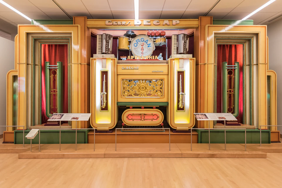 Colorful musical organ display with visible instruments and decorative elements, flanked by informational panels on both sides.