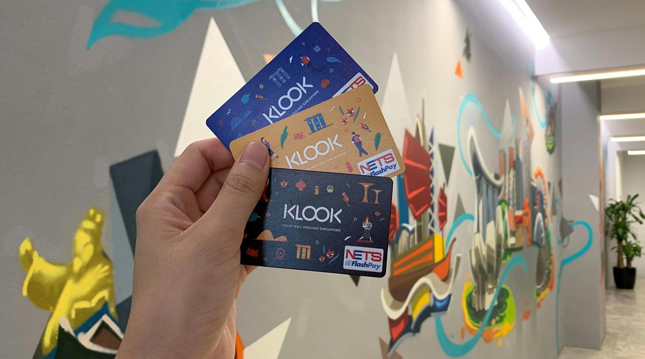 A hand holding three colorful NETS FlashPay cards with a vibrant mural of a cityscape in the background.