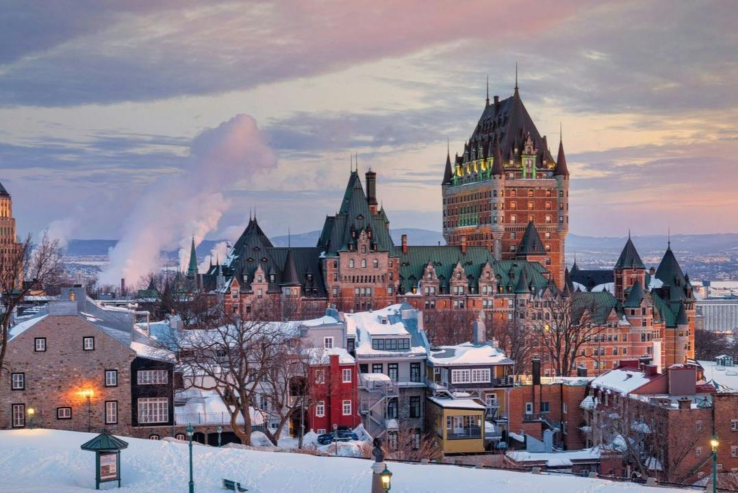 A winter cityscape featuring a historic castle-like building and snow-covered rooftops under a colorful sky.