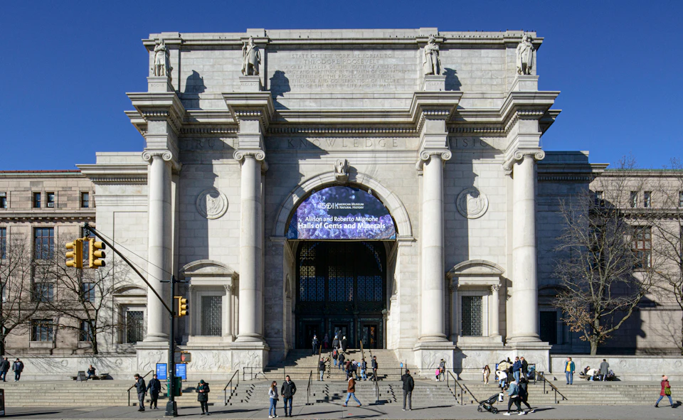 Large, grand entrance of a museum with columns and archways. People walking on the steps. Banner above entrance.