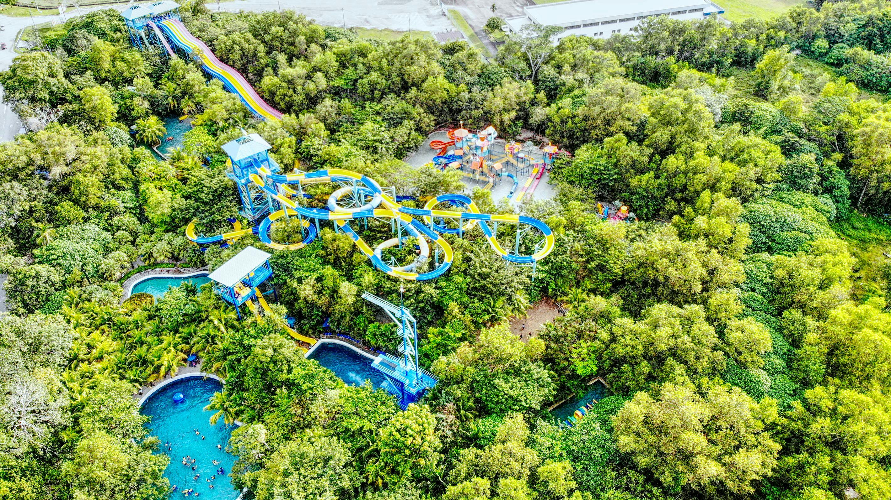 Widok z lotu ptaka na park wodny z kolorowymi zjeżdżalniami, basenami i otaczającymi je zielonymi drzewami.