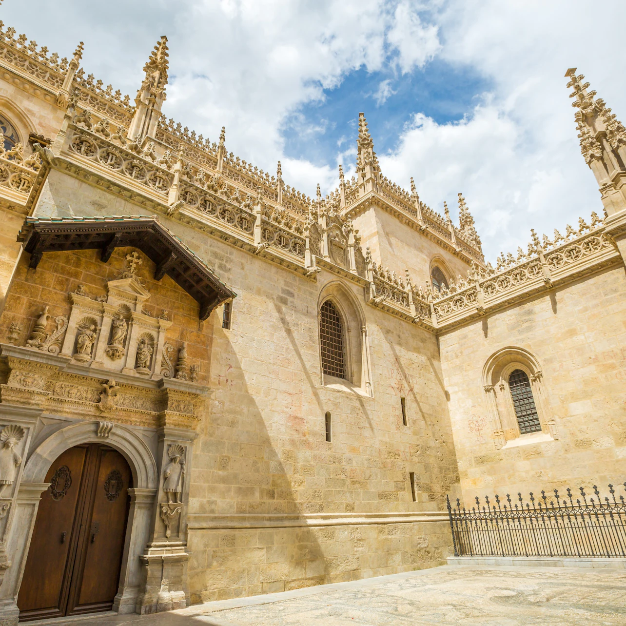 A historic stone building with intricate Gothic details, arched doorways, and decorative spires under a blue sky.