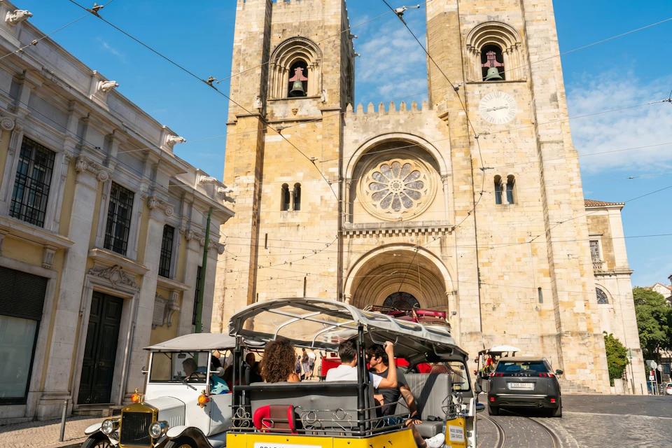 People seated in an open-air tourist vehicle in front of a large historic cathedral with two bell towers and a rose window.