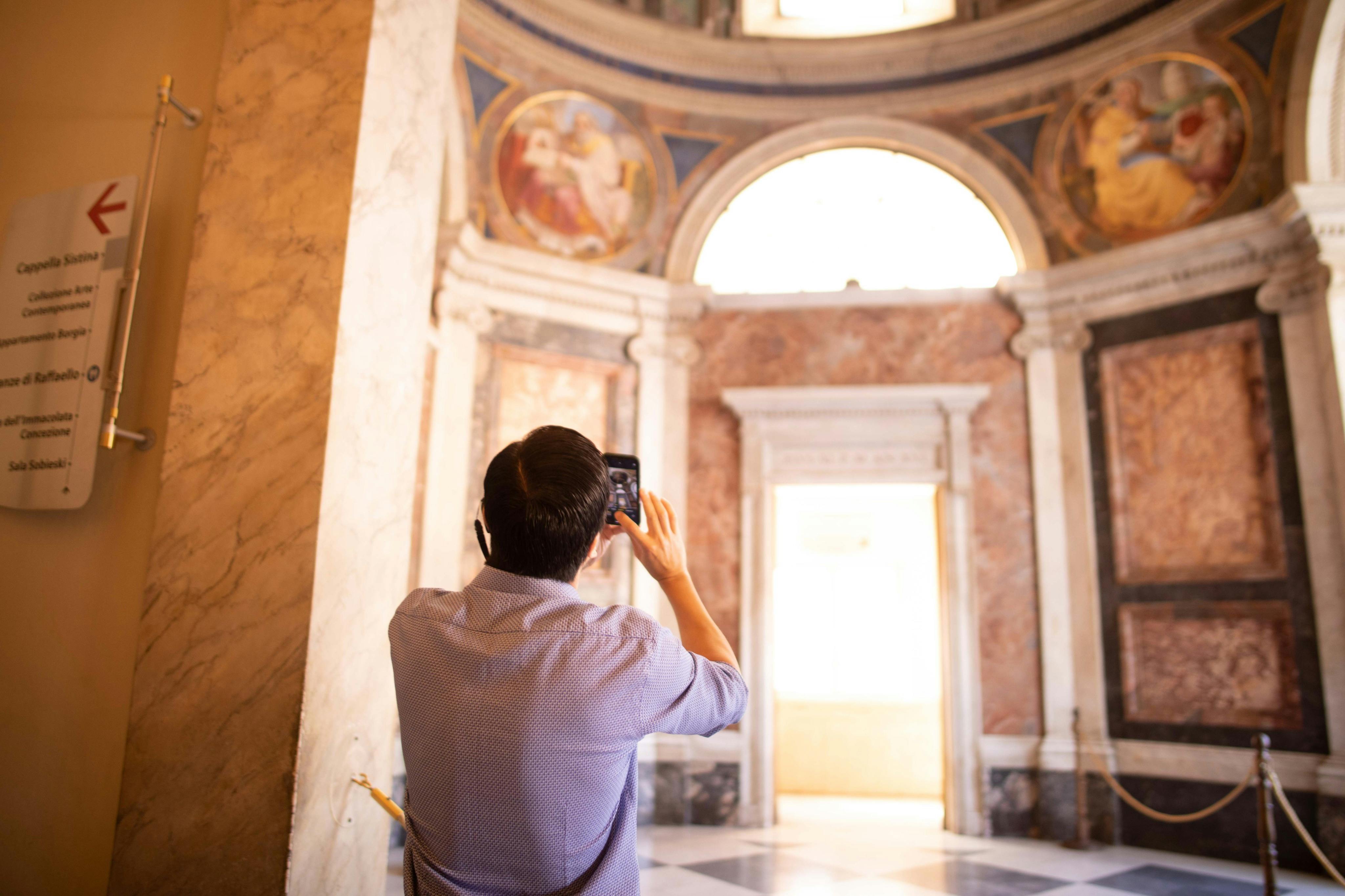 Una persona che scatta una foto con lo smartphone all’interno di un edificio sfarzoso con colonne di marmo e decorazioni murali.